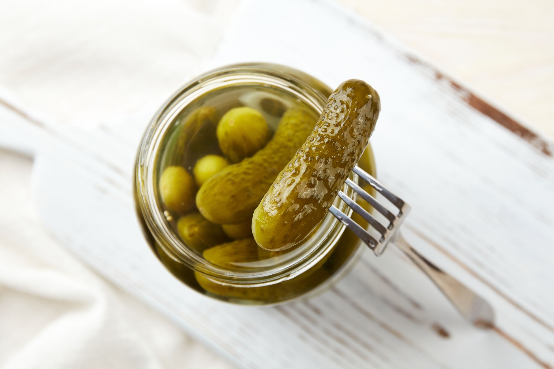 Marinated cucumbers in a jar on a light wooden background.